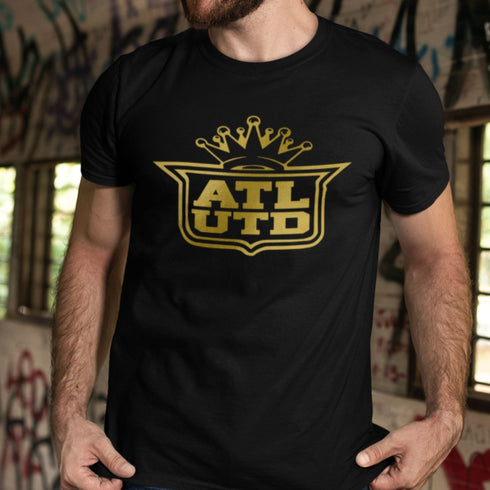 Man wearing a black t-shirt with a yellow 'ATL UTD' logo in an urban setting.