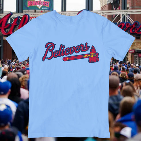 Light blue t-shirt with 'Believers' design in red and black text, worn by a person at a sports event.