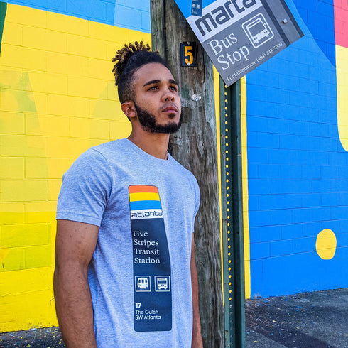 Man wearing a gray t-shirt with a graphic design standing in front of a colorful mural.