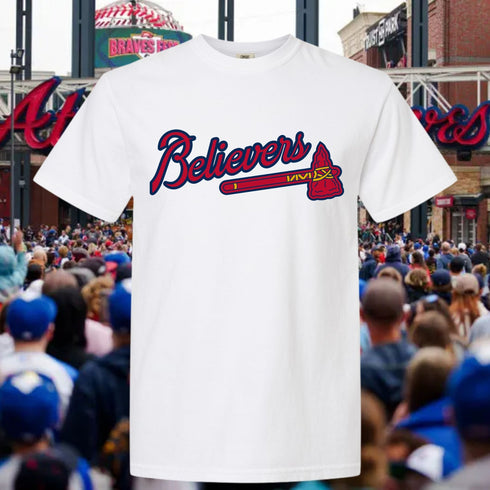 White t-shirt with 'Believers' design in red and blue, worn by a person in a crowd.