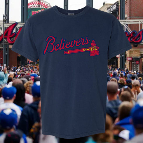 Navy blue t-shirt with 'Believers' design in red and white, set against a sports arena background.