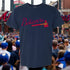 Navy blue t-shirt with 'Believers' design in red and white, set against a sports arena background.