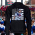 Black hoodie with a graphic of a baseball player on an American flag, worn by a person at a sports event.