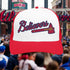 Red and white cap with 'Believers' text and logo over a crowd at a sports event.