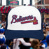 Baseball cap with 'Believers' and bat design in front of a crowd at a sports event.