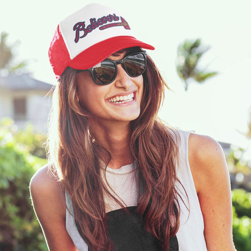 Model wearing red and white Believers Trucker Hat, inspired by Atlanta baseball, adjustable snapback style.