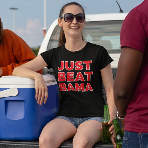 Person wearing a black t-shirt with 'JUST BEAT BAMA' text, sitting on a truck bed with others.