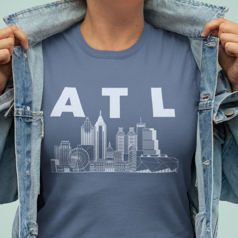 Person wearing a blue t-shirt with 'ATL' and city skyline graphic, holding denim jacket open.