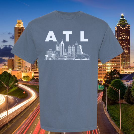 Blue t-shirt with 'ATL' and city skyline graphic against a backdrop of a cityscape at night.
