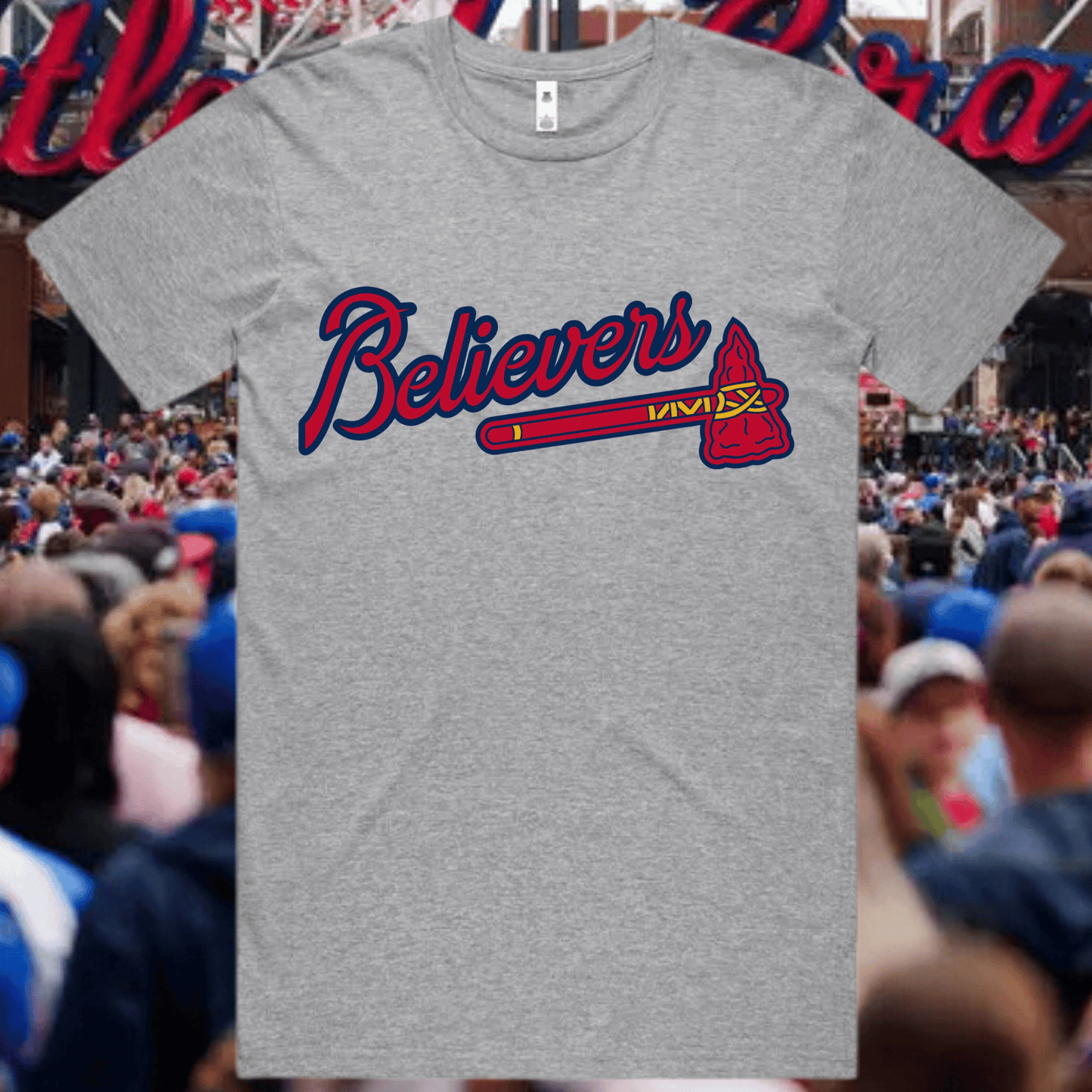 Gray t-shirt with 'Believers' design in red and blue, worn by a person in a crowd.